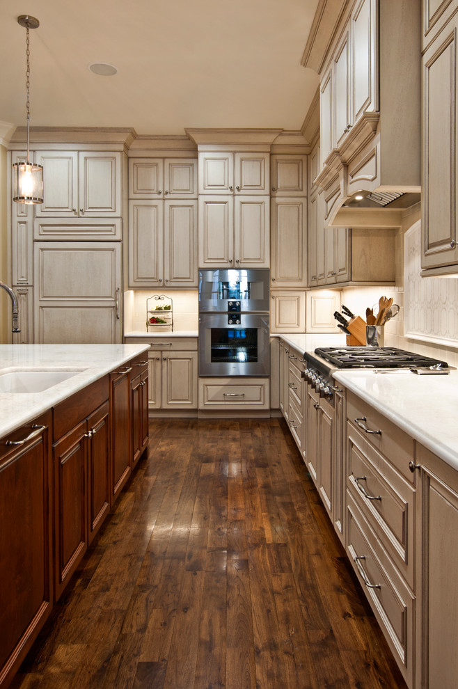 This is an example of a large traditional l-shaped separate kitchen in Nashville with an undermount sink, raised-panel cabinets, beige cabinets, marble benchtops, beige splashback, ceramic splashback, panelled appliances, medium hardwood floors, with island, brown floor and white benchtop.