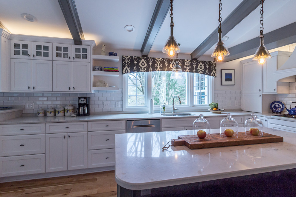 Example of a large transitional u-shaped medium tone wood floor and brown floor enclosed kitchen design with an undermount sink, shaker cabinets, white cabinets, quartzite countertops, white backsplash, subway tile backsplash, stainless steel appliances and an island