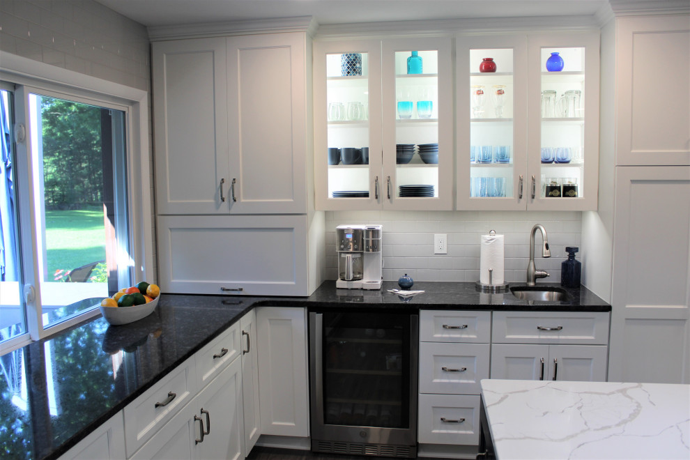 Klassisk inredning av ett stort vit vitt kök, med en undermonterad diskho, blå skåp, bänkskiva i kvarts, grått stänkskydd, stänkskydd i keramik, rostfria vitvaror, en köksö och grått golv