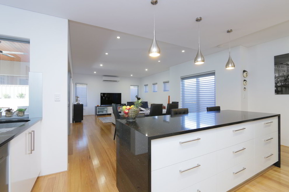 Design ideas for a mid-sized contemporary l-shaped open plan kitchen in Perth with a double-bowl sink, flat-panel cabinets, white cabinets, granite benchtops, white splashback, glass sheet splashback, stainless steel appliances, light hardwood floors and with island.