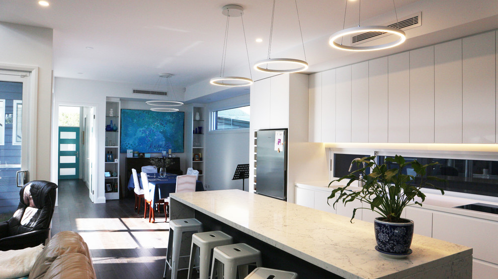 Photo of a large modern galley open plan kitchen in Sydney with an integrated sink, flat-panel cabinets, white cabinets, quartz benchtops, white splashback, window splashback, stainless steel appliances, dark hardwood floors, with island, grey floor and white benchtop.