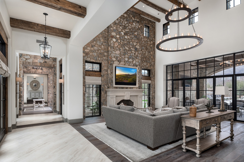 Expansive country open concept family room in Phoenix with multi-coloured walls, dark hardwood floors, a standard fireplace, a stone fireplace surround, a wall-mounted tv, multi-coloured floor, exposed beam and brick walls.