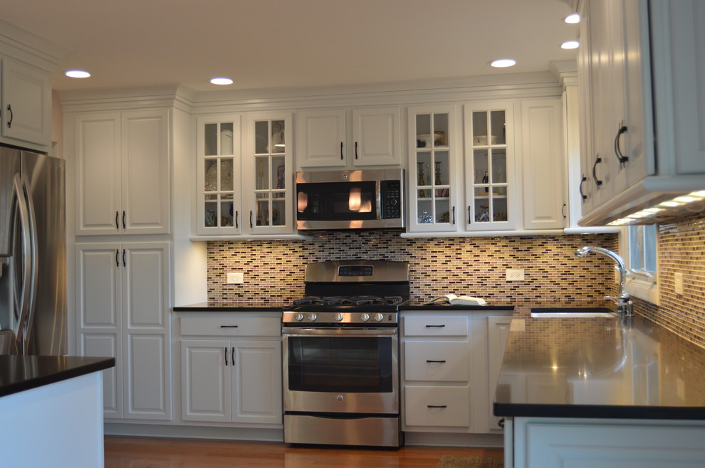 Inspiration for a mid-sized transitional l-shaped medium tone wood floor eat-in kitchen remodel in Chicago with a single-bowl sink, raised-panel cabinets, white cabinets, quartzite countertops, multicolored backsplash, glass tile backsplash, stainless steel appliances and an island