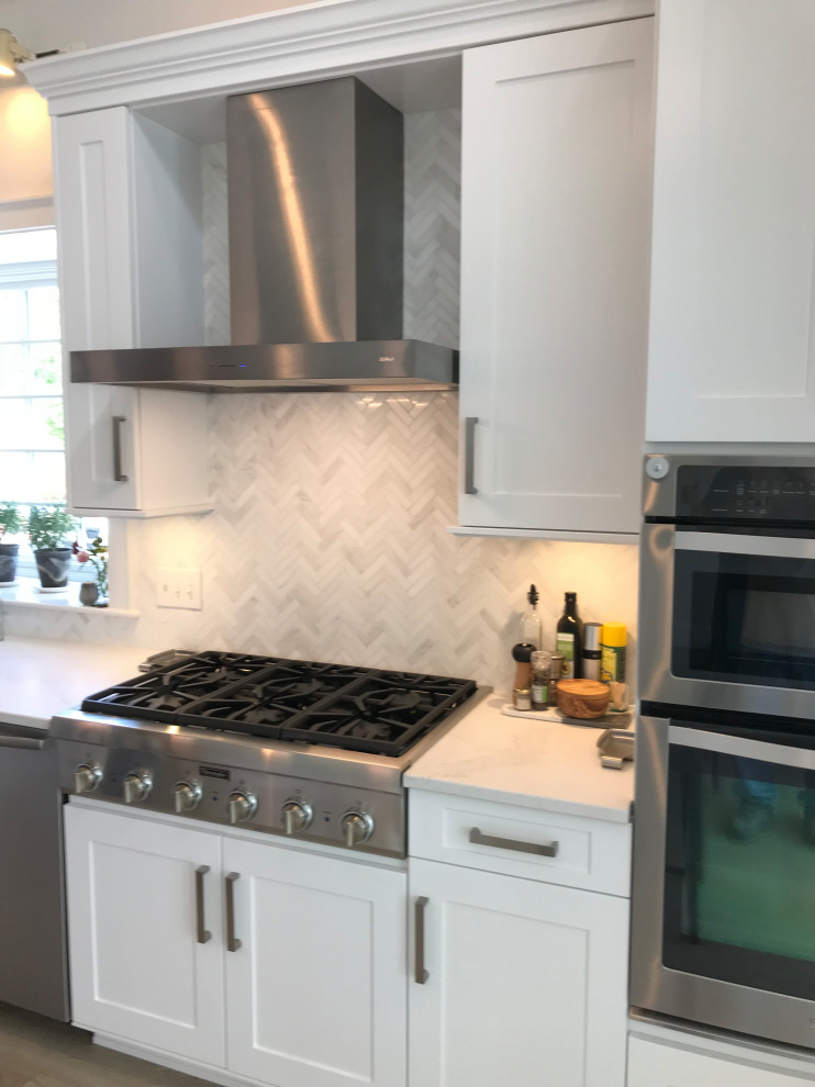 Expansive transitional l-shaped eat-in kitchen in Boston with shaker cabinets, white cabinets, quartzite benchtops, grey splashback, stainless steel appliances, medium hardwood floors, with island and white benchtop.