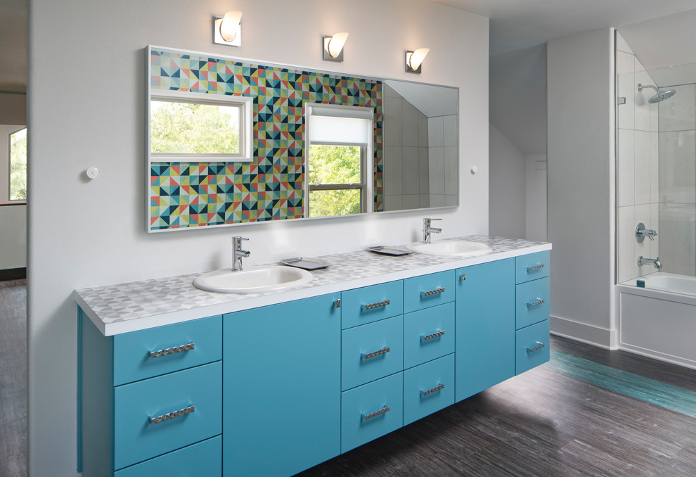 This is an example of a mid-sized midcentury bathroom in Dallas with flat-panel cabinets, blue cabinets, a shower/bathtub combo, white tile, white walls, laminate floors, a drop-in sink, laminate benchtops and brown floor.