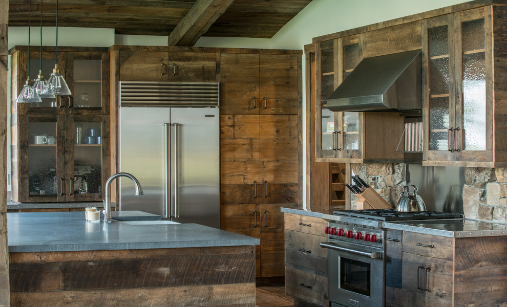 This is an example of a country kitchen in Other with a farmhouse sink, glass-front cabinets, dark wood cabinets, metallic splashback, stainless steel appliances, with island and grey benchtop.