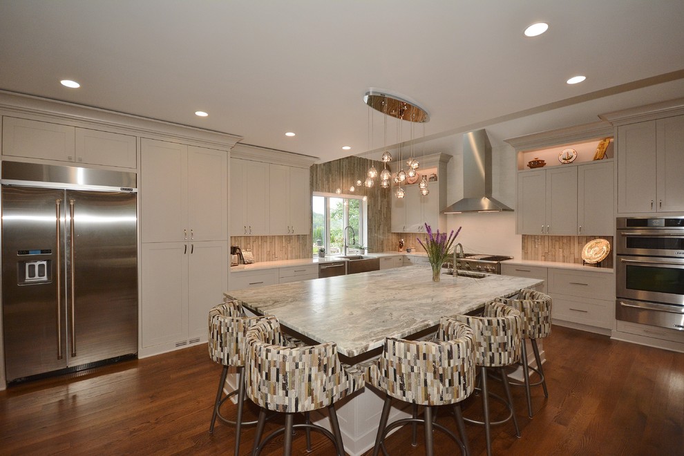 Large transitional u-shaped dark wood floor and brown floor eat-in kitchen photo with a farmhouse sink, recessed-panel cabinets, white cabinets, limestone countertops, beige backsplash, porcelain backsplash, stainless steel appliances, an island and gray countertops