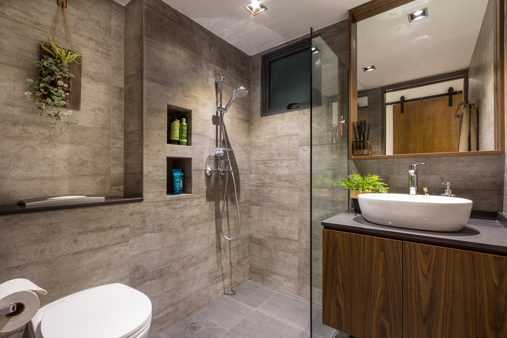 Contemporary bathroom in Singapore with flat-panel cabinets, medium wood cabinets, a curbless shower, a wall-mount toilet, gray tile, grey walls, a vessel sink, grey floor, an open shower and grey benchtops.