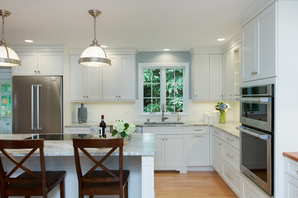 Example of a transitional l-shaped light wood floor eat-in kitchen design in Boston with an undermount sink, recessed-panel cabinets, white cabinets, quartzite countertops, white backsplash, subway tile backsplash, stainless steel appliances and an island