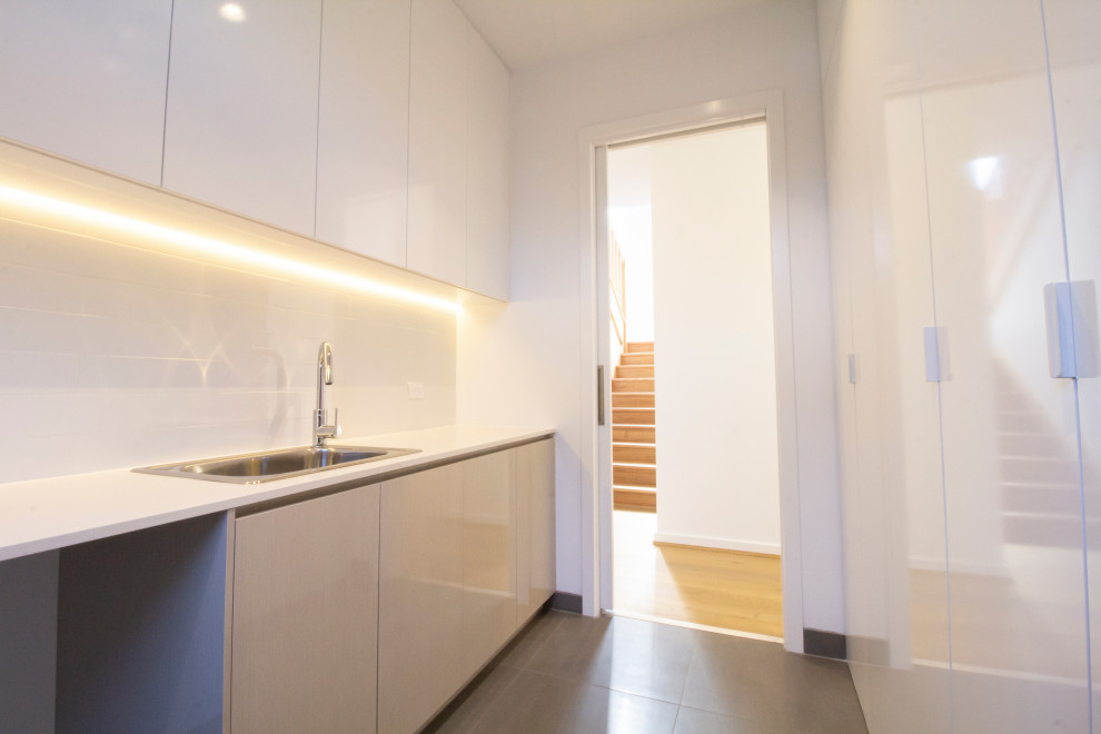 Mid-sized contemporary galley dedicated laundry room in Melbourne with a single-bowl sink, recessed-panel cabinets, white cabinets, concrete benchtops, white walls, ceramic floors, a side-by-side washer and dryer, grey floor and white benchtop.