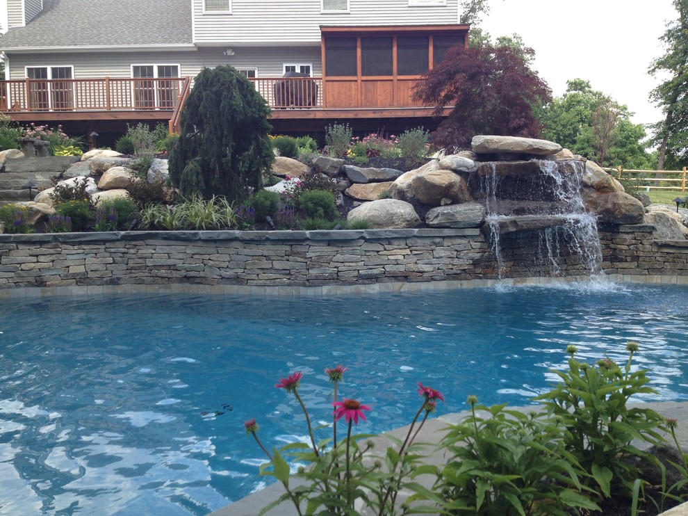Design ideas for a mid-sized traditional backyard custom-shaped lap pool in New York with a water feature and natural stone pavers.