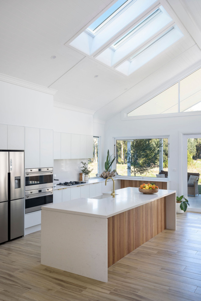 Expansive nautical kitchen/diner in Central Coast with a belfast sink, white cabinets, engineered stone countertops, stainless steel appliances, ceramic flooring, an island, white worktops, a vaulted ceiling, white splashback and engineered quartz splashback.
