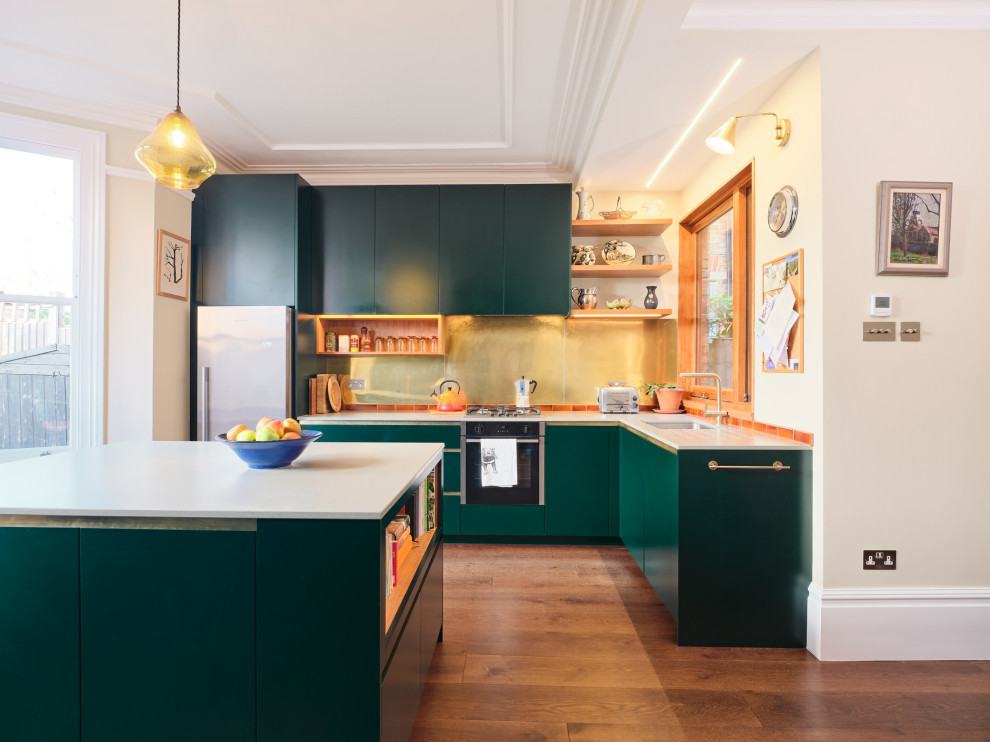 Стильный дизайн: угловая кухня среднего размера в современном стиле с плоскими фасадами, зелеными фасадами, фартуком цвета металлик, островом и белой столешницей - последний тренд