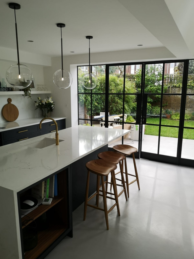 Mid-sized contemporary galley eat-in kitchen in London with a drop-in sink, shaker cabinets, blue cabinets, marble benchtops, white splashback, marble splashback, panelled appliances, concrete floors, with island, grey floor and white benchtop.