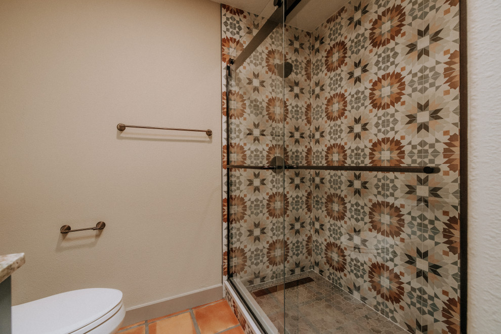 This is an example of a mid-sized master bathroom in Albuquerque with shaker cabinets, blue cabinets, an alcove shower, a one-piece toilet, multi-coloured tile, beige walls, terra-cotta floors, an undermount sink, orange floor, an open shower, multi-coloured benchtops, a niche, a double vanity and a built-in vanity.