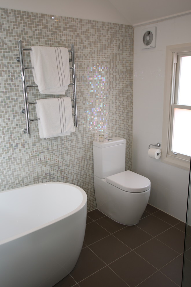 This is an example of a mid-sized contemporary master bathroom in Sydney with recessed-panel cabinets, white cabinets, a freestanding tub, a corner shower, a one-piece toilet, multi-coloured tile, mosaic tile, white walls, porcelain floors, engineered quartz benchtops and an undermount sink.