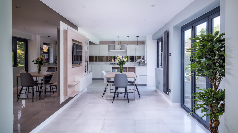 Photo of a contemporary u-shaped open plan kitchen in Berkshire with flat-panel cabinets, solid surface benchtops, brown splashback, mirror splashback, black appliances, ceramic floors, grey floor, a drop-in sink, grey cabinets and white benchtop.