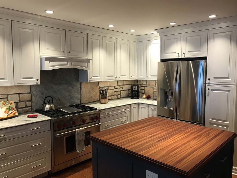 Example of a huge mountain style l-shaped medium tone wood floor and brown floor eat-in kitchen design in New York with an undermount sink, raised-panel cabinets, white cabinets, granite countertops, brown backsplash, stone tile backsplash, stainless steel appliances, an island and gray countertops