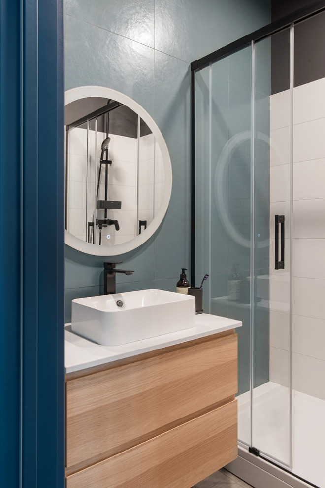 Пример оригинального дизайна: ванная комната среднего размера в стиле лофт с плоскими фасадами, светлыми деревянными фасадами, душем в нише, инсталляцией, синей плиткой, керамогранитной плиткой, серыми стенами, полом из керамической плитки, душевой кабиной, накладной раковиной, столешницей из искусственного кварца, коричневым полом, душем с раздвижными дверями, белой столешницей, зеркалом с подсветкой, тумбой под одну раковину и подвесной тумбой