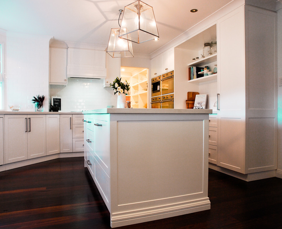 Photo of a mid-sized traditional kitchen in Wollongong with shaker cabinets, quartz benchtops, with island, a farmhouse sink, white cabinets, white splashback, subway tile splashback, stainless steel appliances and dark hardwood floors.