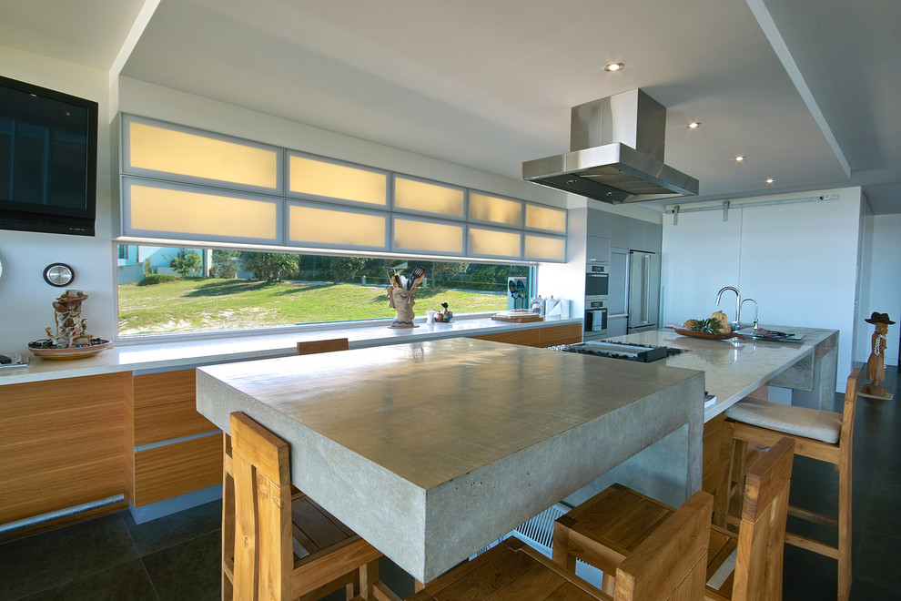 This is an example of a mid-sized beach style galley eat-in kitchen in Brisbane with an undermount sink, glass-front cabinets, light wood cabinets, concrete benchtops, glass sheet splashback and stainless steel appliances.