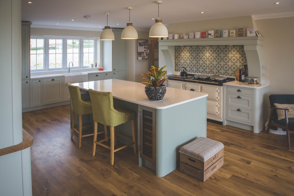 Photo of a large traditional eat-in kitchen in Devon with a farmhouse sink, shaker cabinets, green cabinets, multi-coloured splashback, with island and white benchtop.