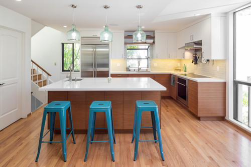 Modern two-tone kitchen with white upper cabinets, warm wood base cabinets, white quartz island, and turquoise bar stools under glass pendant lights