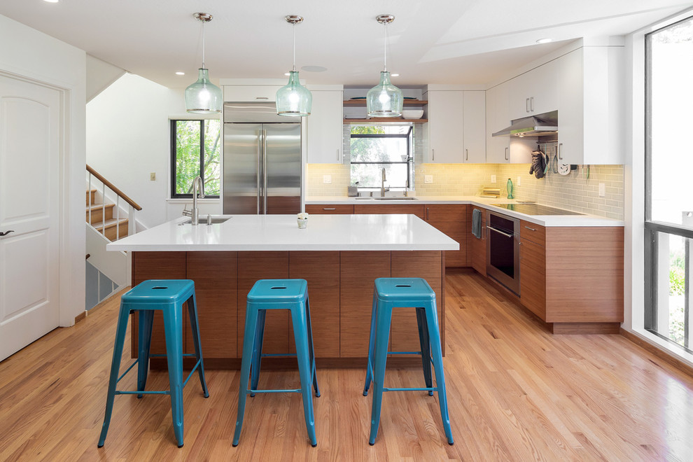 Mid-sized trendy l-shaped medium tone wood floor and brown floor kitchen photo in San Francisco with an undermount sink, flat-panel cabinets, white cabinets, gray backsplash, subway tile backsplash, stainless steel appliances, an island, white countertops and solid surface countertops