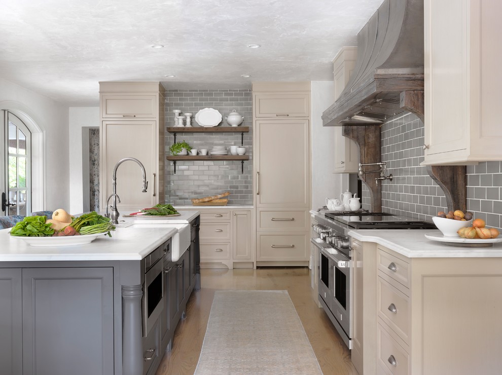 Country l-shaped kitchen in Other with a farmhouse sink, recessed-panel cabinets, beige cabinets, grey splashback, subway tile splashback, stainless steel appliances, medium hardwood floors, with island, brown floor and white benchtop.