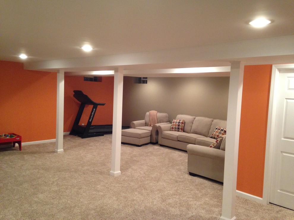 Photo of a large transitional fully buried basement in New York with beige walls, carpet and a standard fireplace.