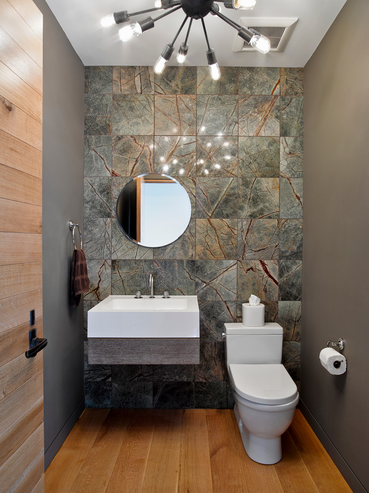 Inspiration for a contemporary powder room in New York with a wall-mount sink, a one-piece toilet, grey walls, medium hardwood floors, marble and gray tile.