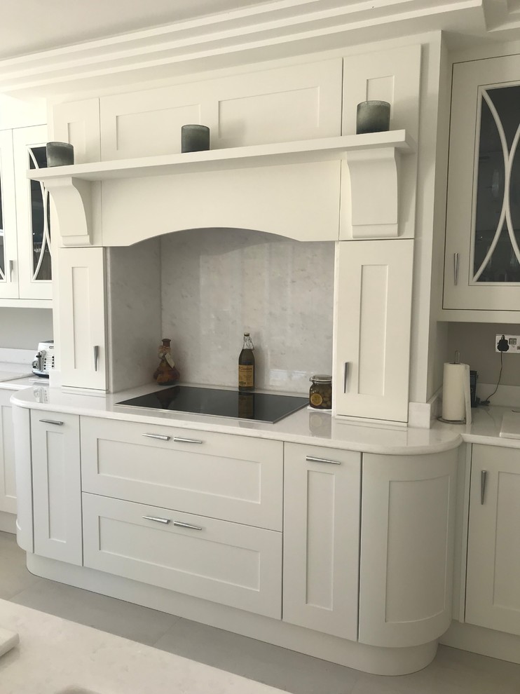 This is an example of a large contemporary open plan kitchen in Hertfordshire with a double-bowl sink, shaker cabinets, white cabinets, quartz worktops, white splashback, stone slab splashback, stainless steel appliances, porcelain flooring, an island, grey floors and white worktops.