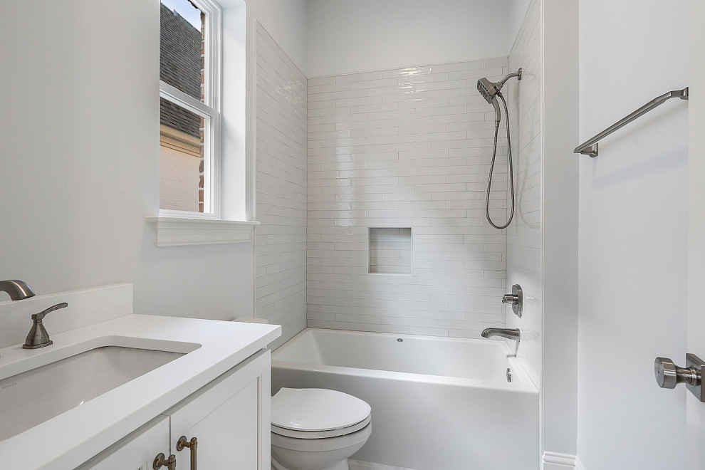 Mid-sized traditional kids bathroom in New Orleans with shaker cabinets, white cabinets, an alcove tub, a shower/bathtub combo, a two-piece toilet, multi-coloured tile, subway tile, grey walls, porcelain floors, an undermount sink, quartzite benchtops, black floor, an open shower, white benchtops, a niche, a double vanity and a built-in vanity.