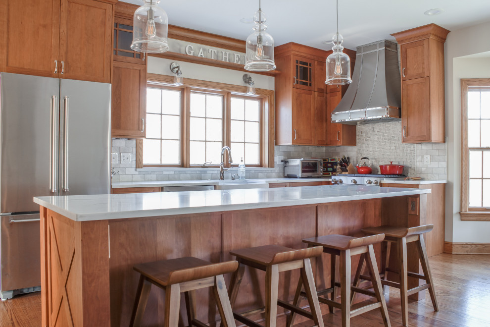 Inspiration for a large transitional l-shaped eat-in kitchen in Detroit with a farmhouse sink, shaker cabinets, medium wood cabinets, quartz benchtops, white splashback, marble splashback, stainless steel appliances, medium hardwood floors, with island, brown floor and white benchtop.