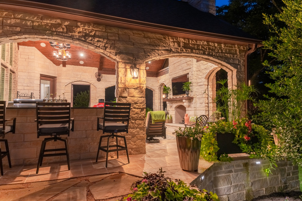Réalisation d'une terrasse arrière tradition de taille moyenne avec une cuisine d'été, des pavés en pierre naturelle et une extension de toiture.
