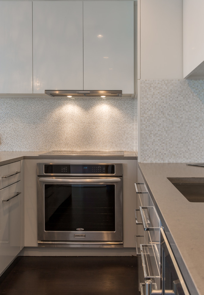 This is an example of a mid-sized contemporary galley kitchen in New York with a single-bowl sink, flat-panel cabinets, beige cabinets, limestone benchtops, beige splashback, mosaic tile splashback, stainless steel appliances, dark hardwood floors and with island.