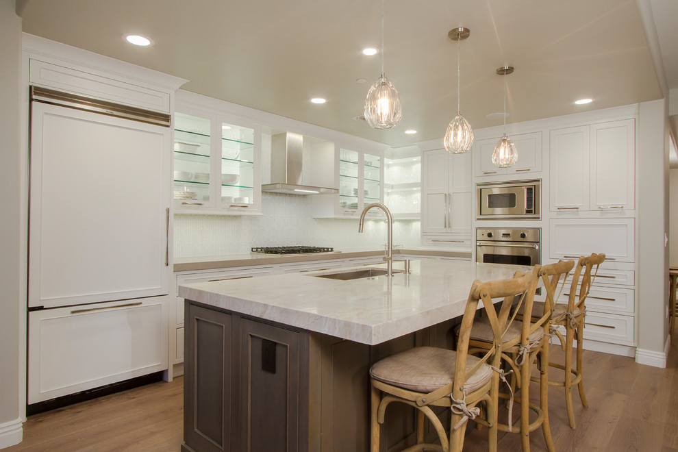 Example of a small transitional l-shaped light wood floor and brown floor eat-in kitchen design in Phoenix with a single-bowl sink, shaker cabinets, white cabinets, quartz countertops, white backsplash, glass tile backsplash, stainless steel appliances, an island and white countertops