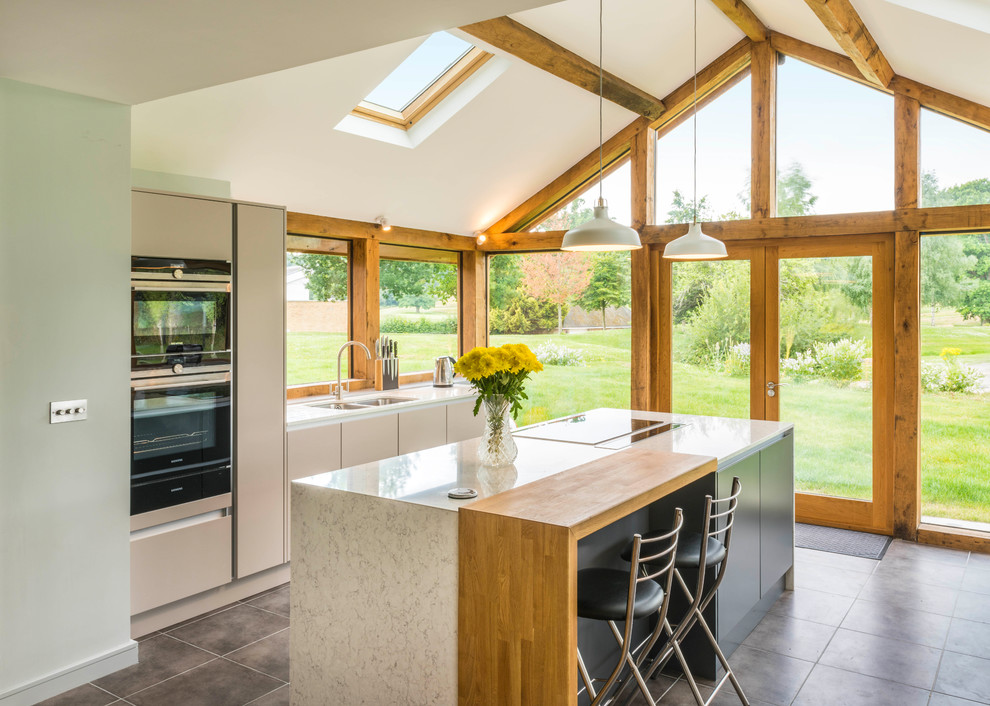 Inspiration for a mid-sized contemporary u-shaped kitchen in Surrey with quartzite benchtops, with island, flat-panel cabinets, grey floor and white splashback.