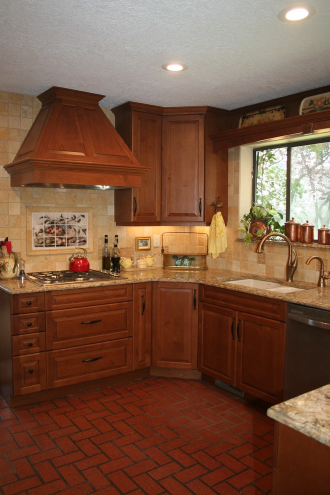 Photo of a mid-sized traditional l-shaped eat-in kitchen in Albuquerque with an undermount sink, raised-panel cabinets, medium wood cabinets, stone tile splashback, brick floors, solid surface benchtops, beige splashback, panelled appliances, red floor and a peninsula.