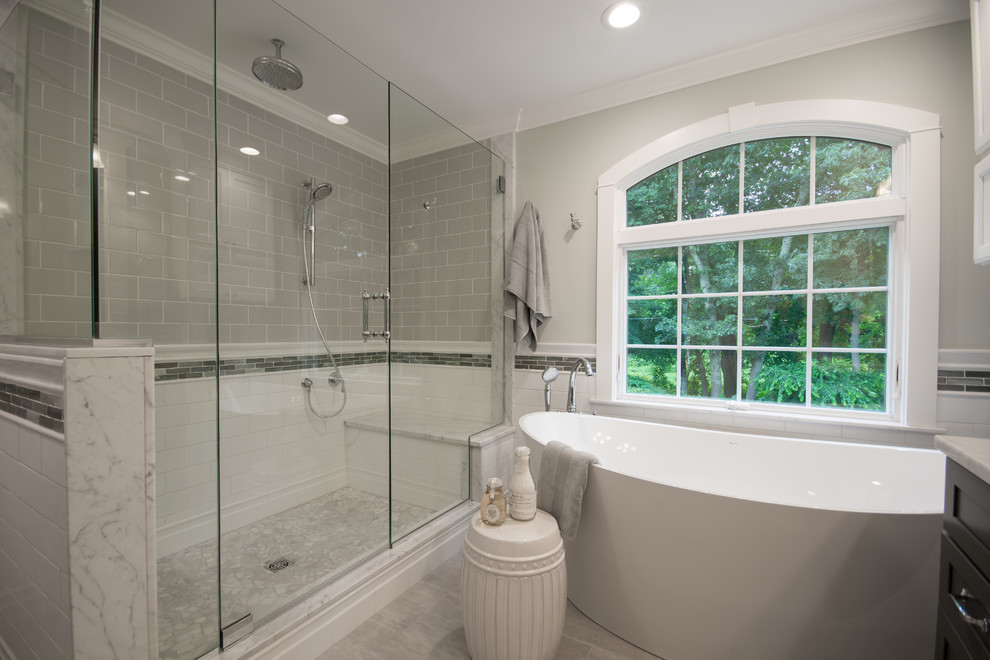 Large traditional master bathroom in Providence with recessed-panel cabinets, dark wood cabinets, a freestanding tub, a corner shower, gray tile, subway tile, grey walls, porcelain floors, an undermount sink, granite benchtops, grey floor, a hinged shower door and grey benchtops.