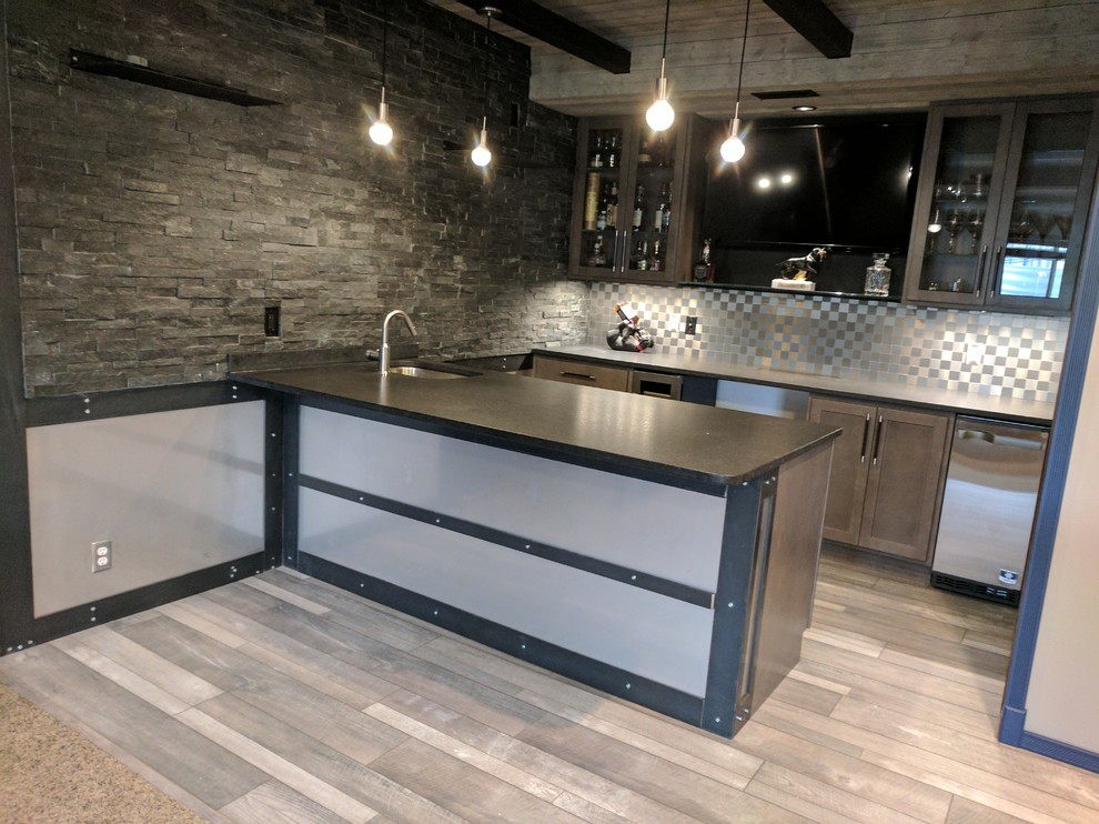 This is an example of a mid-sized industrial u-shaped wet bar in Omaha with an undermount sink, shaker cabinets, grey cabinets, granite benchtops, grey splashback, metal splashback, light hardwood floors and grey floor.