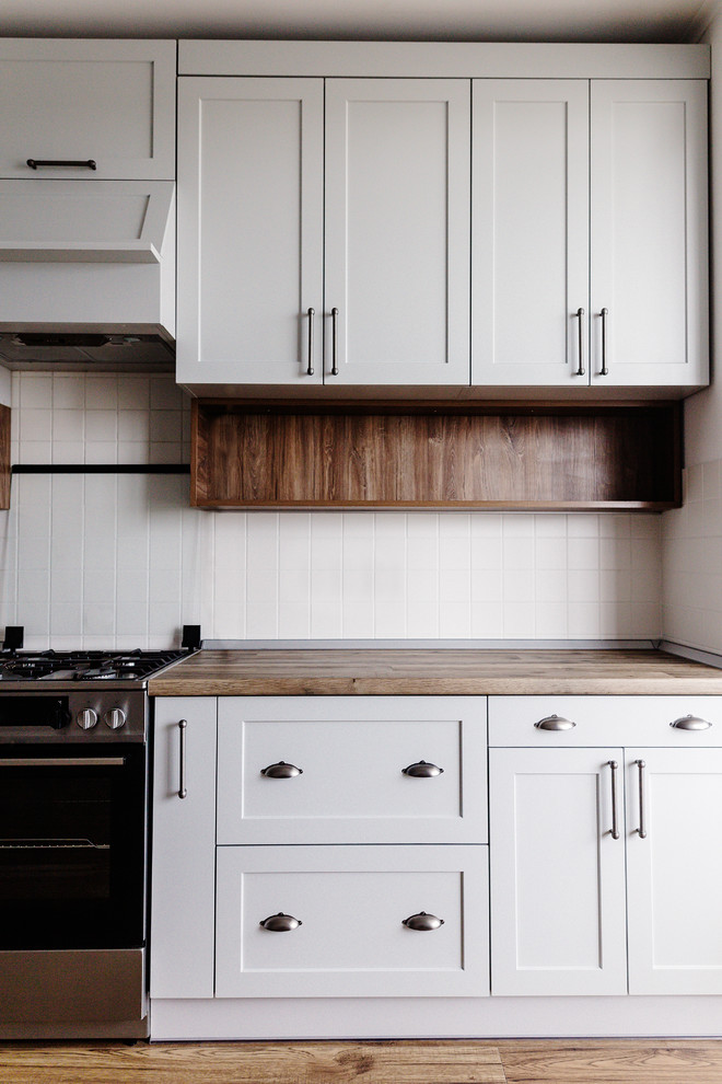 Inspiration for a mid-sized transitional u-shaped dark wood floor and brown floor eat-in kitchen remodel in DC Metro with a drop-in sink, recessed-panel cabinets, white cabinets, wood countertops, white backsplash, ceramic backsplash, stainless steel appliances, a peninsula and brown countertops