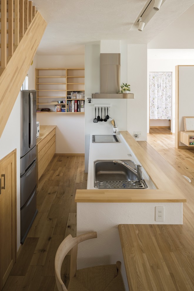 This is an example of a scandinavian open plan kitchen in Other with a single-bowl sink, beaded inset cabinets, light wood cabinets, solid surface benchtops, white appliances, medium hardwood floors, no island, brown floor and white benchtop.