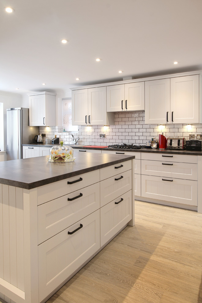 Photo of a large transitional galley eat-in kitchen in Sussex with a single-bowl sink, recessed-panel cabinets, grey cabinets, laminate benchtops, white splashback, ceramic splashback, panelled appliances, vinyl floors and with island.