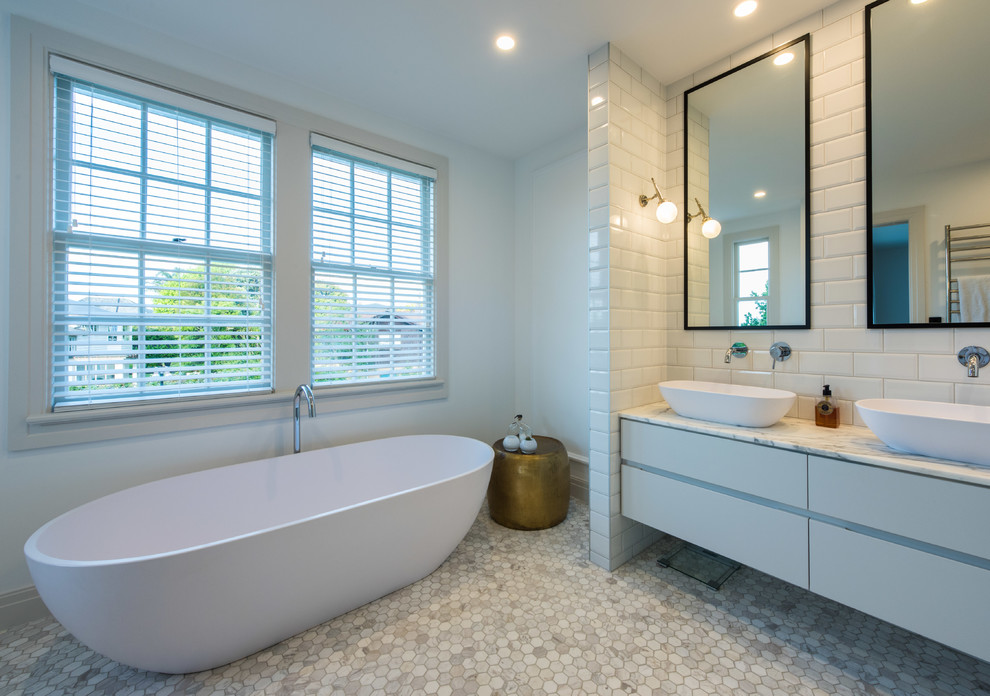 Photo of a large transitional bathroom in Auckland with flat-panel cabinets, white cabinets, a freestanding tub, an alcove shower, a one-piece toilet, white tile, subway tile, white walls, mosaic tile floors, a vessel sink, tile benchtops, grey floor and a hinged shower door.