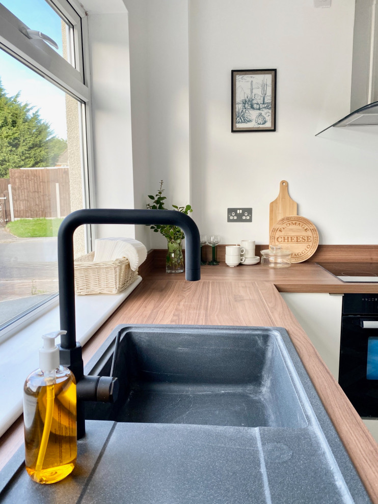 Design ideas for a small contemporary l-shaped separate kitchen in Gloucestershire with an integrated sink, flat-panel cabinets, white cabinets, wood benchtops, brown splashback, timber splashback, black appliances, linoleum floors, no island, multi-coloured floor and brown benchtop.
