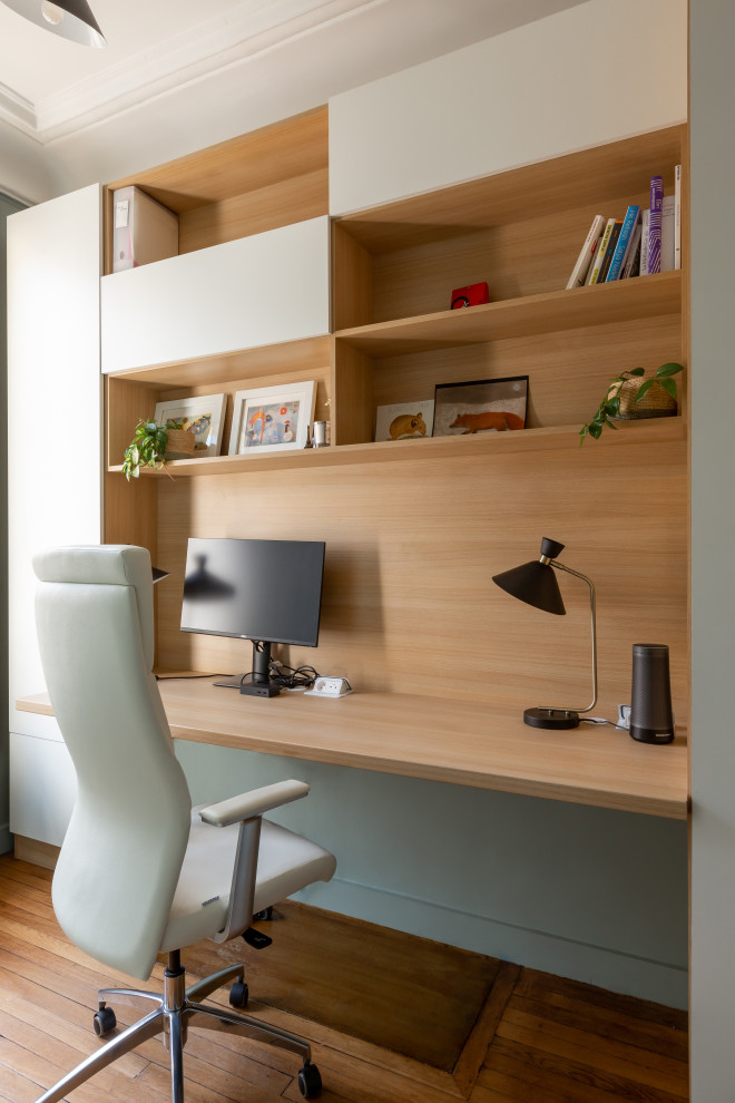 Großes Modernes Arbeitszimmer ohne Kamin mit Arbeitsplatz, grüner Wandfarbe, hellem Holzboden, freistehendem Schreibtisch und braunem Boden in Paris