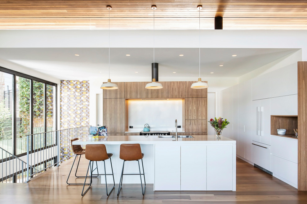Design ideas for a contemporary u-shaped open plan kitchen in Sydney with a drop-in sink, flat-panel cabinets, white cabinets, quartz benchtops, white splashback, panelled appliances, medium hardwood floors, with island, brown floor, white benchtop and wood.