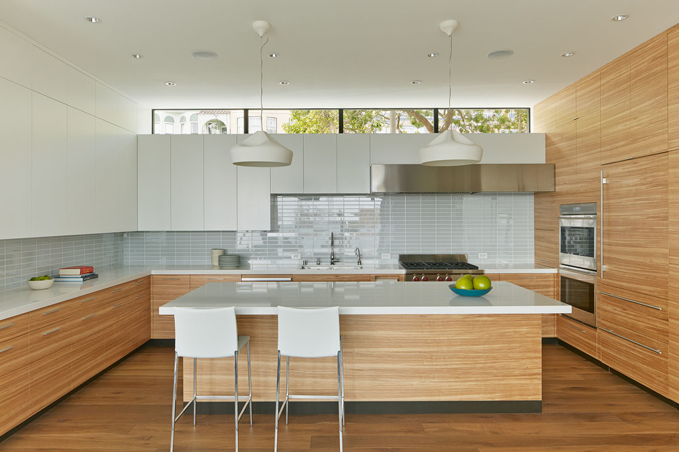 Photo of a contemporary u-shaped kitchen in San Francisco with flat-panel cabinets, medium wood cabinets, grey splashback, panelled appliances, medium hardwood floors and with island.