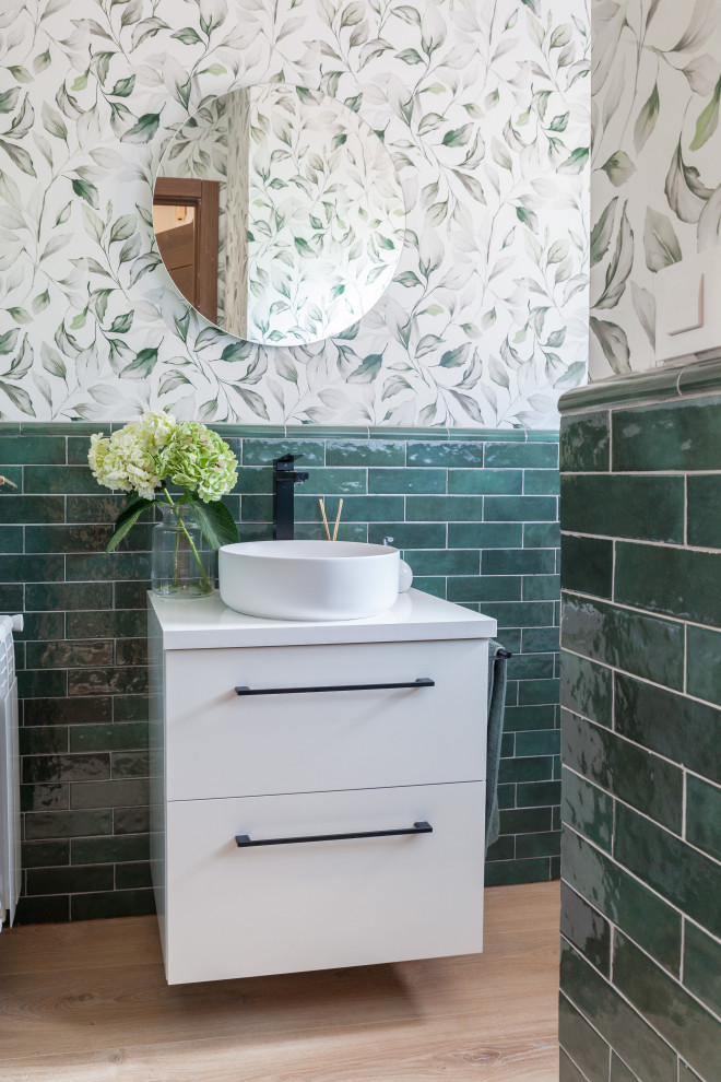 Small trendy green tile and ceramic tile medium tone wood floor, brown floor and wallpaper powder room photo in Other with flat-panel cabinets, white cabinets, a two-piece toilet, white walls, a vessel sink, white countertops and a floating vanity
